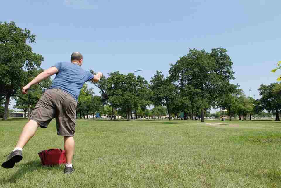A man learning how to throw a disc golf disc properly.