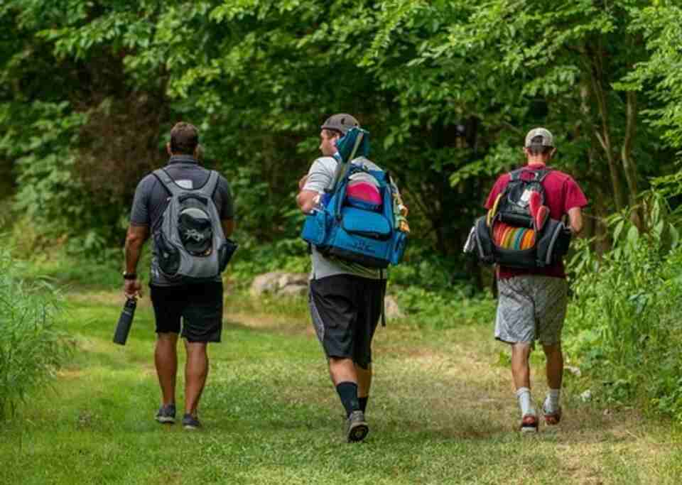 Three friends walking to a disc golf course.