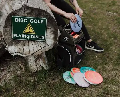 A person with a backpack full of discs, getting ready to play disc golf.