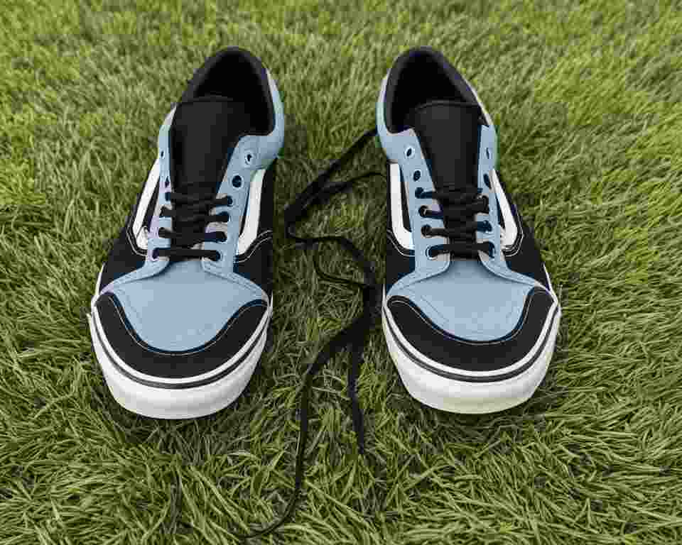A pair of Vans shoes sit on the disc golf course grass, displaying their worn soles and laces untied.