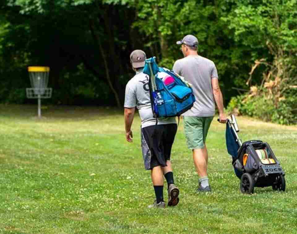 A couple of disc golfers hauling their disc golf bags along the course.